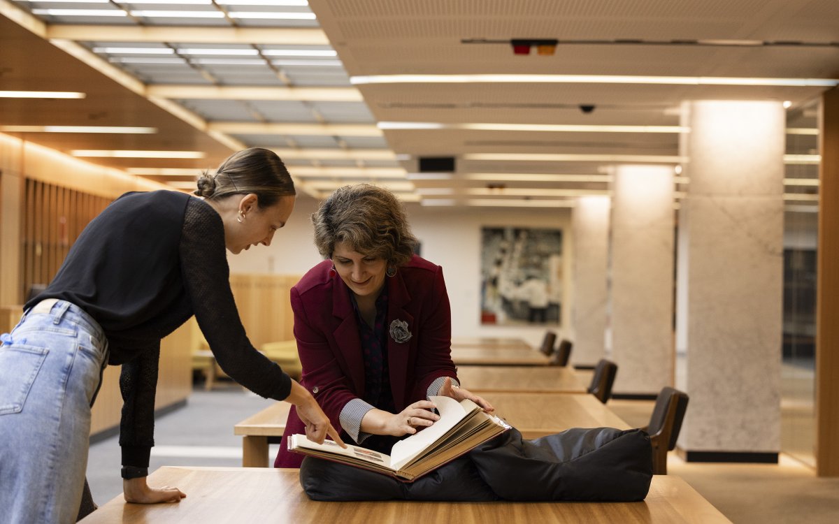 Two people bending over a desk and looking at a book.